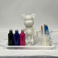 Fluid art bear next to 3 bottles of vibrant pouring paints and pouring supplies