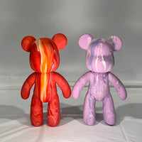 two fluid art bears side by side, one is red orange and yellow, the other is pink lilac and white